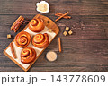 Cinnamon rolls on a wooden table, accompanied by cinnamon sticks and burnt sugar, traditional autumn and winter dessert for the cold season. Ideal as a design template or for a shop window display, 143778609