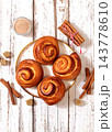 Delicious hot buns rolls on a wooden table, accompanied by cinnamon sticks and burnt sugar, traditional autumn and winter dessert for the cold season. Ideal as a design template 143778610