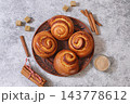 Cinnamon rolls on concrete table, accompanied by cinnamon sticks and burnt sugar, traditional autumn and winter dessert for the cold season. Ideal as a design template or for a shop window display, 143778612