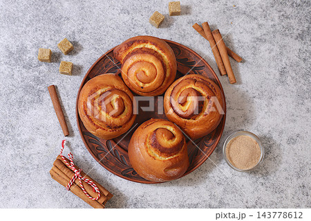 Cinnamon rolls on concrete table, accompanied by cinnamon sticks and burnt sugar, traditional autumn and winter dessert for the cold season. Ideal as a design template or for a shop window display, Cinnamon rolls on concrete table, accompanied by cinnamon sticks and burnt sugar, traditional autumn and winter dessert for the cold season. Ideal as a design template or for a shop window display, 143778612