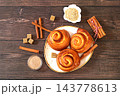 Delicious hot buns rolls on a wooden table, accompanied by cinnamon sticks and burnt sugar, traditional autumn and winter dessert for the cold season. Ideal as a design template 143778613