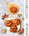 Delicious hot buns rolls on concrete table, accompanied by cinnamon sticks and burnt sugar, traditional autumn and winter dessert for the cold season. Ideal as a design template 143778614