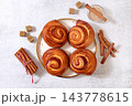 Delicious hot buns rolls on concrete table, accompanied by cinnamon sticks and burnt sugar, traditional autumn and winter dessert for the cold season. Ideal as a design template 143778615