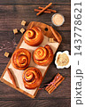 Cinnamon rolls on a wooden table, accompanied by cinnamon sticks and burnt sugar, traditional autumn and winter dessert for the cold season. Ideal as a design template or for a shop window display, 143778621