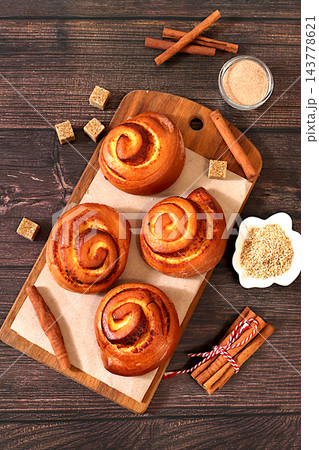 Cinnamon rolls on a wooden table, accompanied by cinnamon sticks and burnt sugar, traditional autumn and winter dessert for the cold season. Ideal as a design template or for a shop window display, 143778621