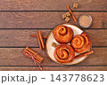 Cinnamon rolls on a wooden table, accompanied by cinnamon sticks and burnt sugar, traditional autumn and winter dessert for the cold season. Ideal as a design template or for a shop window display, 143778623
