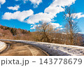 old country road in Carpathian mountains of Ukraine. landscape in late winter. trees on the roadside in morning light. blue sky with fluffy clouds above the distant ridge. travel background old country road in Carpathian mountains of Ukraine. landscape in late winter. trees on the roadside in morning light. blue sky with fluffy clouds above the distant ridge. travel background 143778679