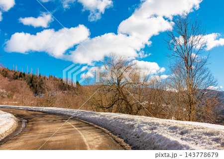 old country road in Carpathian mountains of Ukraine. landscape in late winter. trees on the roadside in morning light. blue sky with fluffy clouds above the distant ridge. travel background old country road in Carpathian mountains of Ukraine. landscape in late winter. trees on the roadside in morning light. blue sky with fluffy clouds above the distant ridge. travel background 143778679