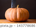 orange pumpkin on the wooden table. autumn vegetable harvest. dark background for thanksgiving or halloween carving concept. huge old knife stick in the vegetable orange pumpkin on the wooden table. autumn vegetable harvest. dark background for thanksgiving or halloween carving concept. huge old knife stick in the vegetable 143778686