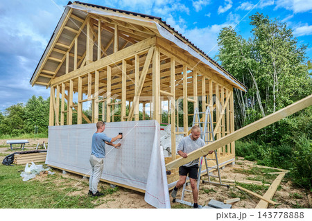 Worker fixes windproof membrane to timber frame with staple gun as structure takes shape. Worker fixes windproof membrane to timber frame with staple gun as structure takes shape. 143778888