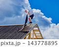 Installing corrugated asphalt roofing sheets, construction worker positions new panel beside completed section of pitched timber roof. 143778895