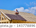 Installation of corrugated asphalt roofing sheets on timber rafters, construction worker positions panels across sloping roof during house building. 143778896