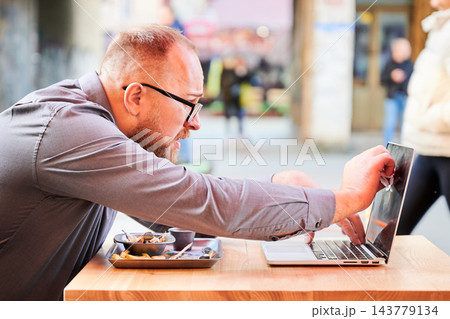 Man cleaning laptop screen with napkin while eating at outdoor cafe, focused freelancer maintaining device during lunch break, hygiene and remote work concept Man cleaning laptop screen with napkin while eating at outdoor cafe, focused freelancer maintaining device during lunch break, hygiene and remote work concept 143779134