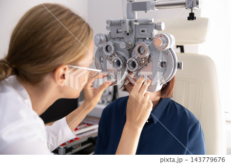 Optometrist adjusting phoropter during patient eye examination in ophthalmology clinic 143779676