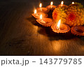 Diwali diyas glowing beside festive flowers on a wooden surface 143779785