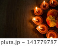 Diwali diyas glowing beside orange flowers on dark wooden surface 143779787