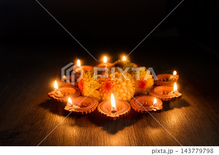 Diwali diyas glowing around festive flowers on a dark wooden floor 143779798