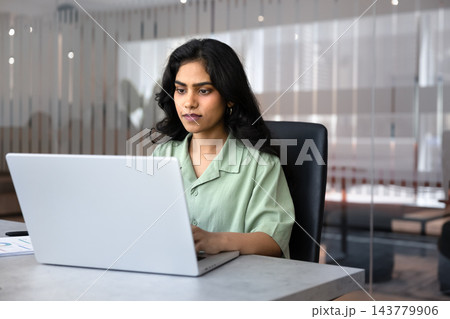 Serious South Asian businesswoman reviewing project details, working on laptop 143779906