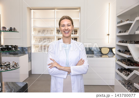 Portrait of optician standing with arms crossed in optical store 143780077