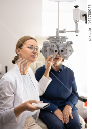 Optometrist performing eye examination for senior woman 143780078