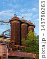 Vertical photo of historic blast furnace cowper stoves rusty steel towers dome tops service walkways green tree leaves and blue sky in Duisburg Ruhr region North Rhine Westphalia Germany 143780263