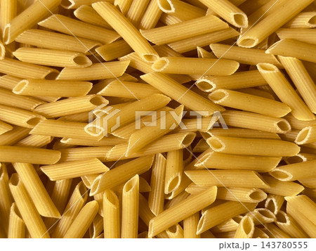 Raw penne pasta heap on a dark background. Dry uncooked penne pasta, textured background. Raw penne pasta heap on a dark background. Dry uncooked penne pasta, textured background. 143780555
