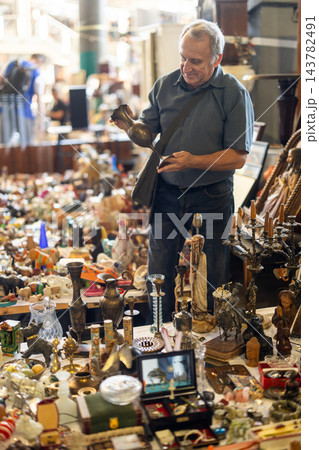 Elderly man is choosing vintage bronze vase at an outdoor flea market 143782491
