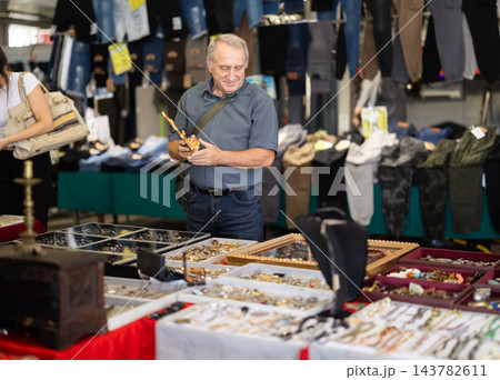 Senior man buyer is examining used crucifix at flea market 143782611