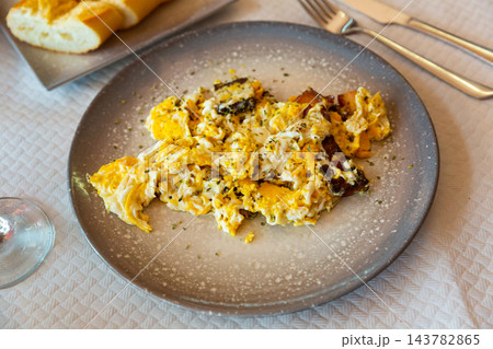 Tasty scrambled eggs with bacon on plate served with cutlery 143782865