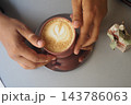 Hands holding a cup of coffee with latte art at a table 143786063