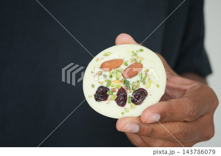 Hand holding a round white dessert topped with almonds and pistachios Hand holding a round white dessert topped with almonds and pistachios 143786079
