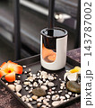 Ceramic Essential Oil Burner with Candle Flame, Pebbles, and Plumeria Flowers in Spa Setting 143787002