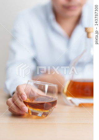 man with glass of cognac on table, suffering from alcohol addiction and alcoholism concept. depicting emotional distress, depression, substance abuse problem, unhealthy lifestyle and mental health 143787300