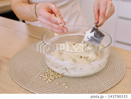 Kneading dough. Culinary work. Female baker hand adding flour mixing ingredient in glass bowl preparing healthy cookies with pine nuts. Kneading dough. Culinary work. Female baker hand adding flour mixing ingredient in glass bowl preparing healthy cookies with pine nuts. 143790335