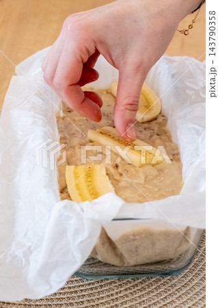 Cake making. Fruit pastry. Female confectioner hand adding pieces to dough in baking dish parchment on table cooking sweet banana bread. Cake making. Fruit pastry. Female confectioner hand adding pieces to dough in baking dish parchment on table cooking sweet banana bread. 143790358
