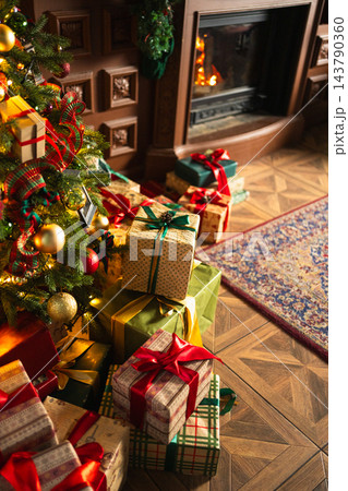 Many gift boxes in classical Christmas decorated interior living room library with fireplace. Christmas gift near fir tree. Modern classic style interior design apartment. Christmas eve at home 143790360