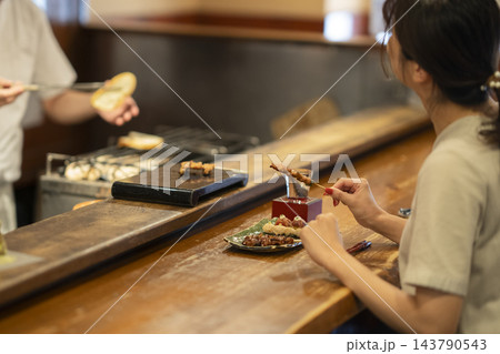 焼き鳥屋のカウンター席で焼き鳥と日本酒を嗜む若い女性の一人客の後ろ姿 143790543