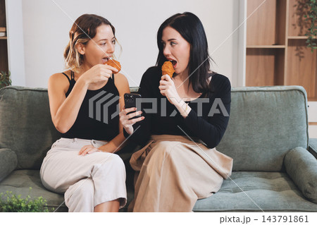 Two young female students using a laptop while sitting on a sofa at home. Student life concept with studying, teamwork, and online learning. Two young female students using a laptop while sitting on a sofa at home. Student life concept with studying, teamwork, and online learning. 143791861
