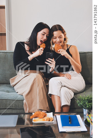 Two young female students using a laptop while sitting on a sofa at home. Student life concept with studying, teamwork, and online learning. Two young female students using a laptop while sitting on a sofa at home. Student life concept with studying, teamwork, and online learning. 143791862