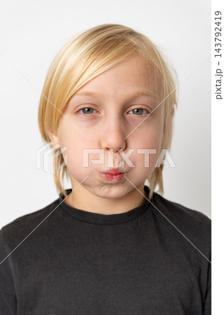Child with blonde hair and blue eyes making a playful expression with puffed cheeks and pursed lips, looking directly into the camera on a white background Child with blonde hair and blue eyes making a playful expression with puffed cheeks and pursed lips, looking directly into the camera on a white background 143792419