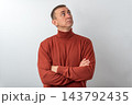 Thoughtful man in a red turtleneck with arms crossed, looking up and pondering future plans, decisions and ideas against a plain studio background, copy space for text 143792435