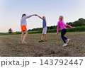 Mother, girl and a boy barefoot and holding hands, dancing and running through a rural field at sunset, captured in warm summer evening light, joyful and carefree 143792447