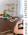 Young boy intently playing dominoes with another person at a wooden table indoors, focused on placing tiles in a quiet family moment of learning, strategy and bonding 143792453