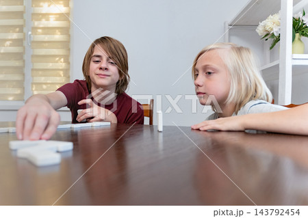 Two young boys are sitting at a wooden table, engaging in a game of dominoes, focusing on placing pieces and developing their playing strategy during leisure time Two young boys are sitting at a wooden table, engaging in a game of dominoes, focusing on placing pieces and developing their playing strategy during leisure time 143792454