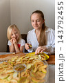 Woman and smiling child making homemade dried apple snacks together, arranging fruit slices on a dehydrator tray, sharing a happy and healthy cooking experience 143792455