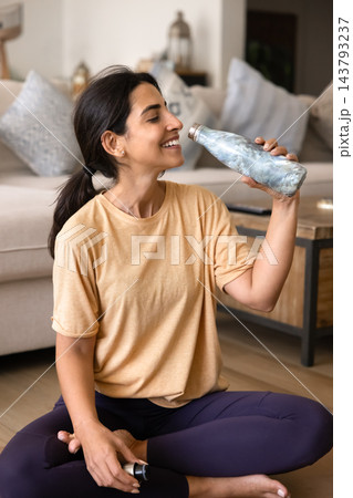 Smiling young lady resting on floor with opened fitness bottle Smiling young lady resting on floor with opened fitness bottle 143793237