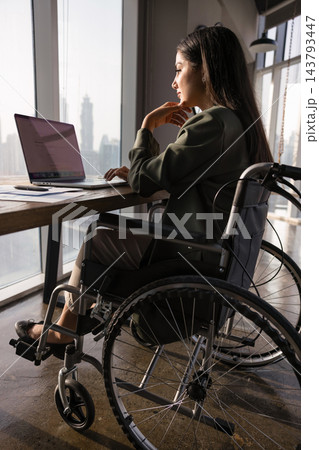Latina woman with disability sitting in wheelchair working on laptop 143793447