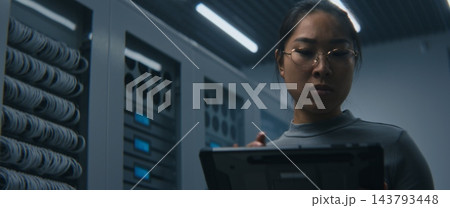 IT Engineer Examining High Density Network Ports, Cable Connections While Reviewing Data on Tablet IT Engineer Examining High Density Network Ports, Cable Connections While Reviewing Data on Tablet 143793448