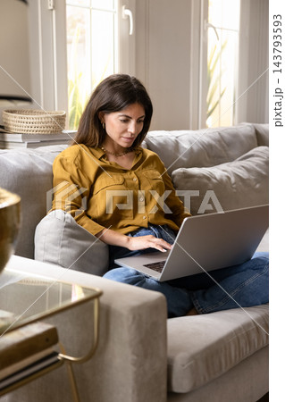Woman focused on remote work using laptop on couch 143793593