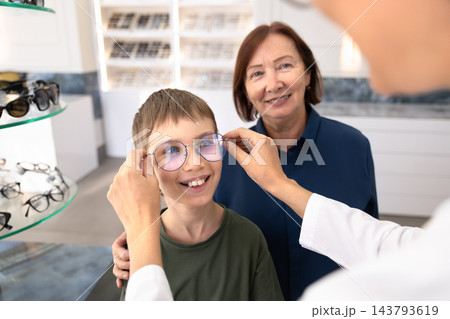 Female ophthalmologist putting new eyeglasses on child 143793619